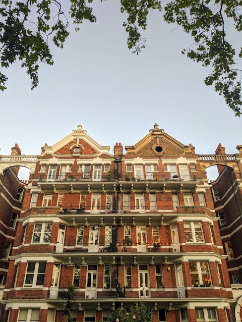 A multi-storey residential building constructed with red brick and white stone detailing, featuring multiple balconies with metal railings and large sash windows. The building has decorative gables an